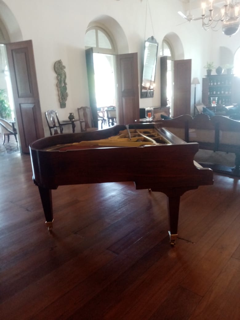 Polished mahogany grand piano installed in a colonial manor living room with timber flooring