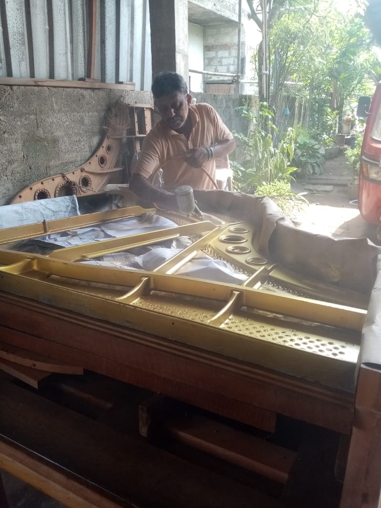 Craftsman applying gold lacquer gilding to a cast-iron piano harp in the Welisara workshop