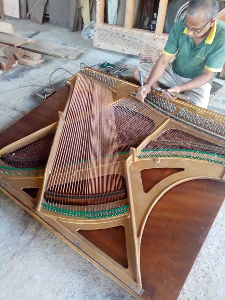 Piano restorer installing copper-wound bass strings on a gold acoustic piano harp